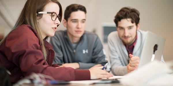 three students sitting around a laptop.